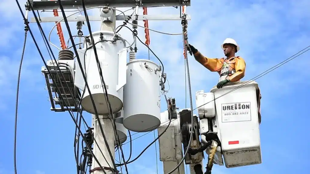 Mains gantées tenant un tournevis près d'une boîte d'interrupteur ouverte avec fils électriques visibles