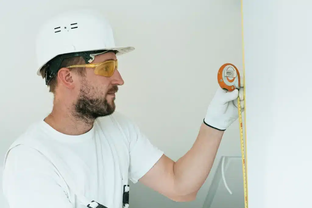 Mains mesurant l'intérieur d'un tiroir avec un mètre ruban rigide, outils de mesure à proximité.