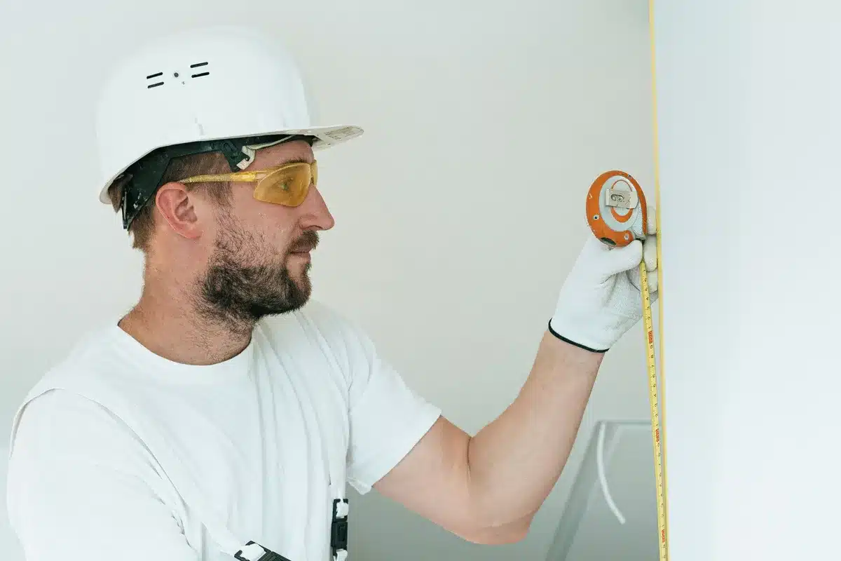 Mains mesurant l'intérieur d'un tiroir avec un mètre ruban rigide, outils de mesure à proximité.