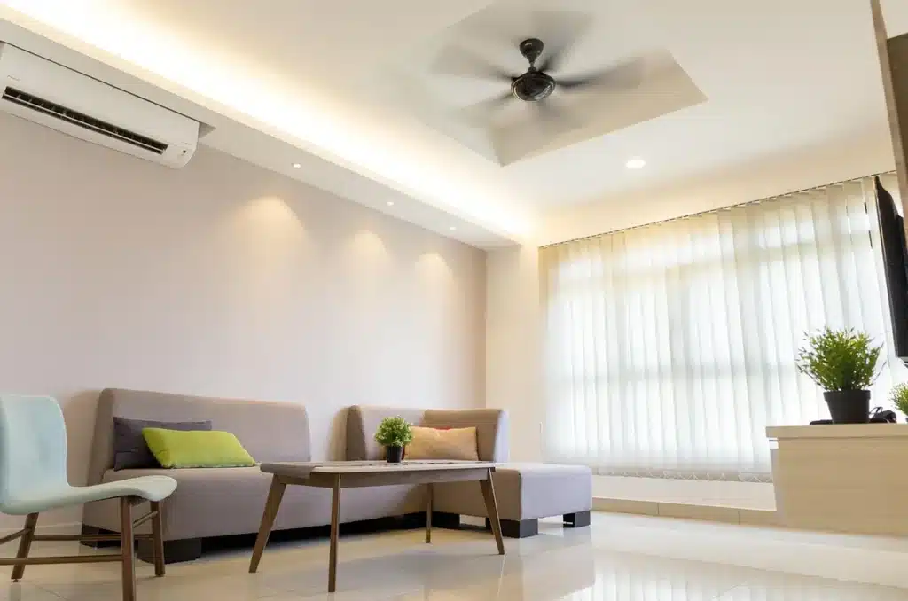 Climatiseur mobile posé près d'une fenêtre dans un salon lumineux, avec une main ajustant la télécommande