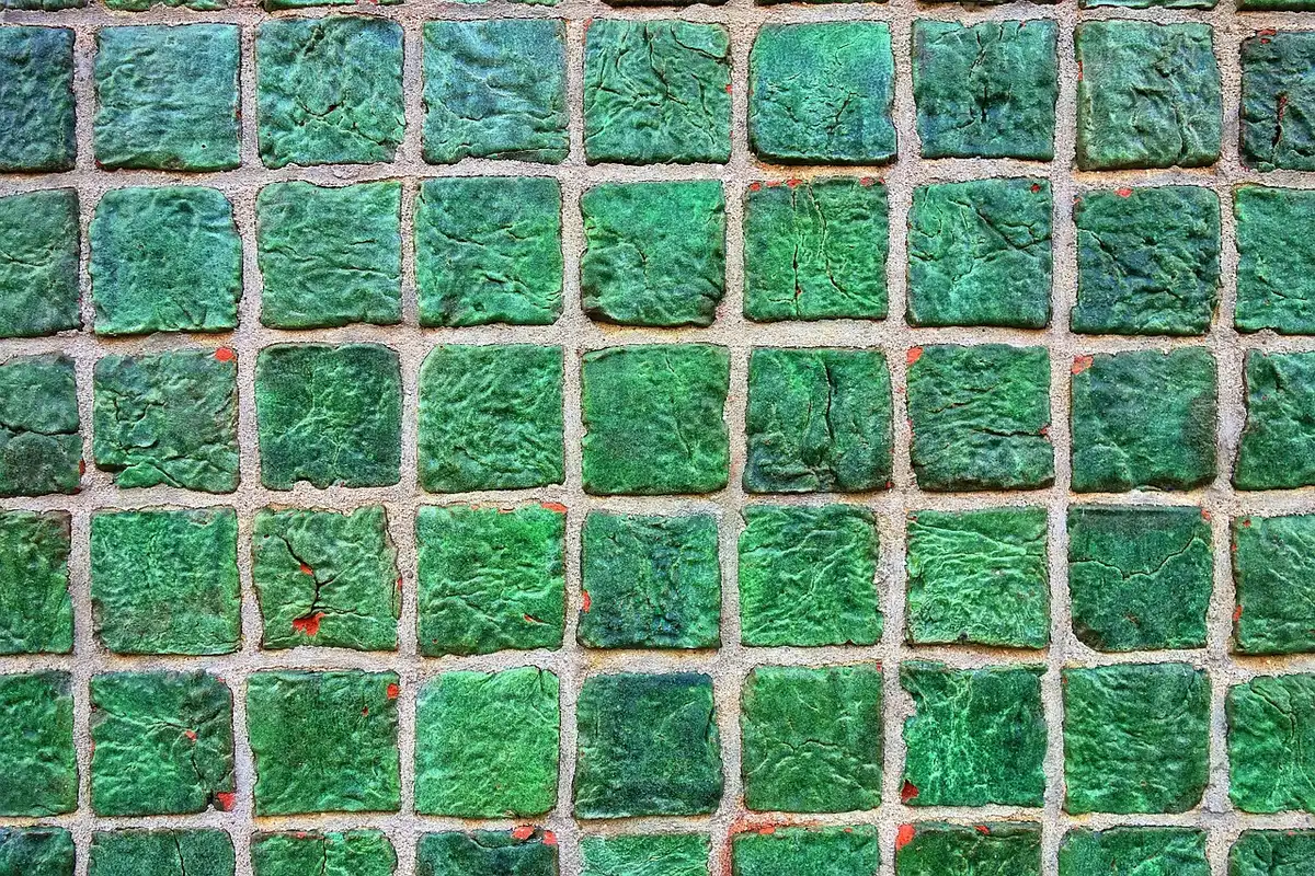Main gantée utilisant un grattoir en plastique sur un joint de carrelage, lumière du jour